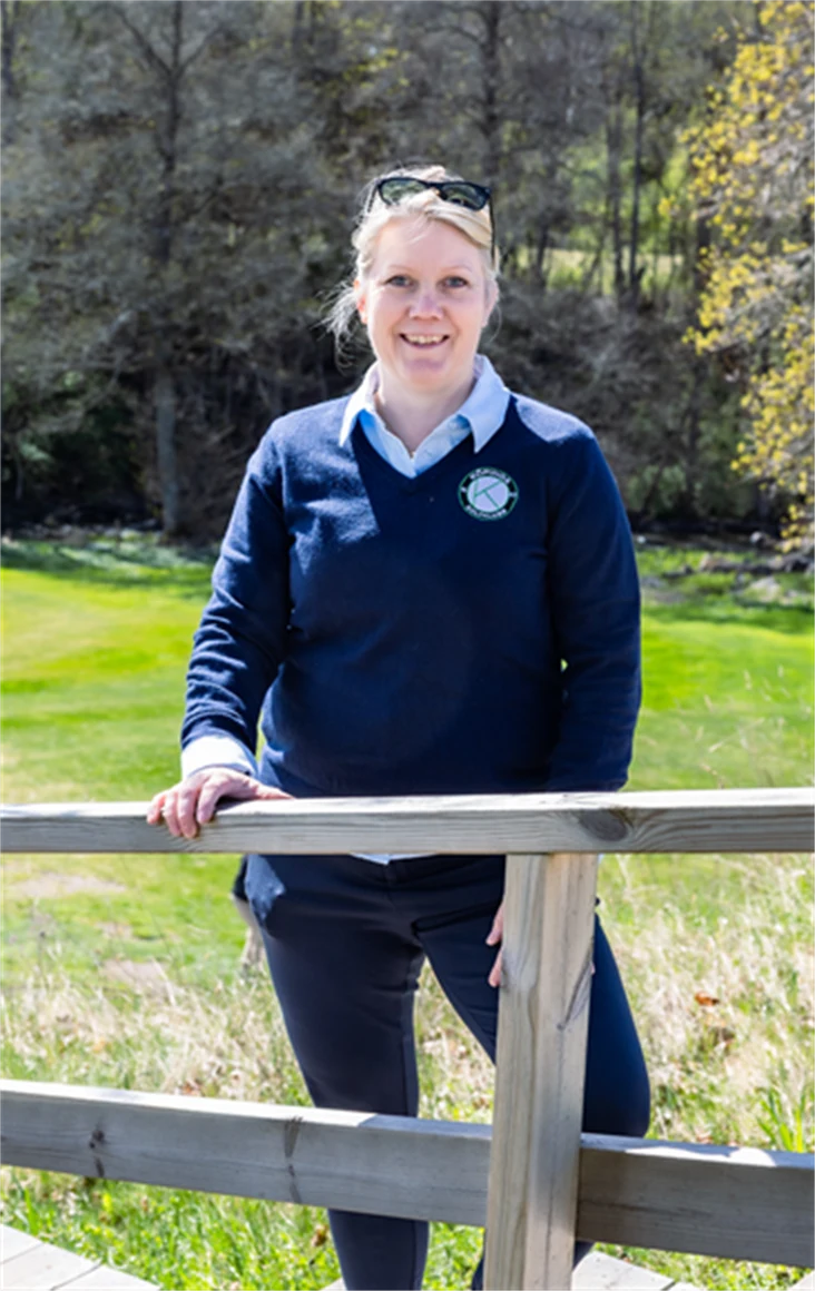 Bild på Lena Björkdahl som är klubbchef för Köpings Golfklubb. Hon står utomhus vid golfbanan.